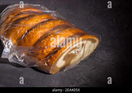 Ungewöhnlicher zweifarbiger frischer Laib Brot in einer transparenten Plastiktüte auf schwarzem Hintergrund, Foto in einem niedrigen Schlüssel bei hartem Licht, Nahaufnahme Stockfoto