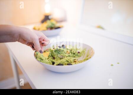 Weibliche Hand Dipping Nachos in Guacamole Sauce mit Oliven Stockfoto