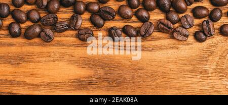 Kaffeebohnen aus nächster Nähe auf einem Tisch aus strukturierten Holzbrettern verstreut. Stockfoto