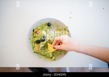 Weibliche Hand Dipping Nachos in Guacamole Sauce mit Oliven Stockfoto