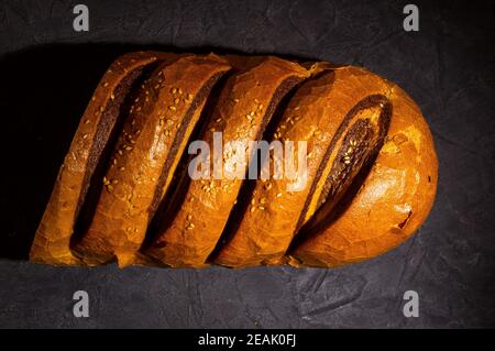 Ungewöhnlicher zweifarbiger frischer Laib Brot auf schwarzem Hintergrund, Foto in einer niedrigen Taste bei hartem Licht, Nahaufnahme Stockfoto