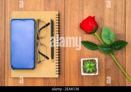 Bild von oben von Handy auf Notizblock und roter Rose Auf Holztisch Stockfoto