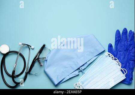 Blaue Stoffkappe, medizinische Einwegmaske, Handschuhe und Plastikbrille auf blauem Hintergrund Stockfoto