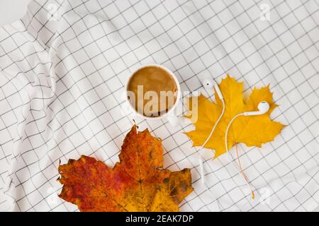 Herbstkomposition. Tasse kaffeetasse, Herbstblätter und Kopfhörer auf weißem kariertem Tuch. Flach liegend, Draufsicht, Kopierbereich Stockfoto