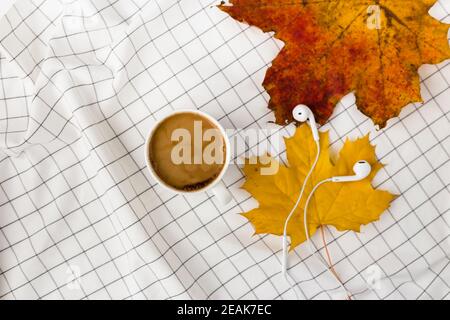 Herbstkomposition. Tasse kaffeetasse, Herbstblätter und Kopfhörer auf weißem kariertem Tuch. Flach liegend, Draufsicht, Kopierbereich Stockfoto