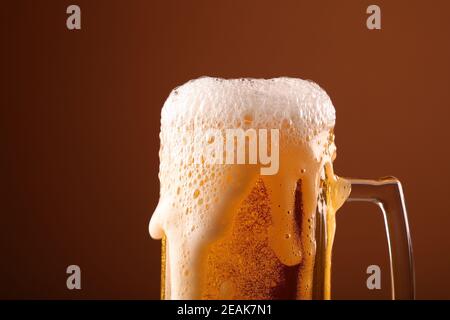 Nahaufnahme Gießen schaumig Bier in Glas über braun Stockfoto