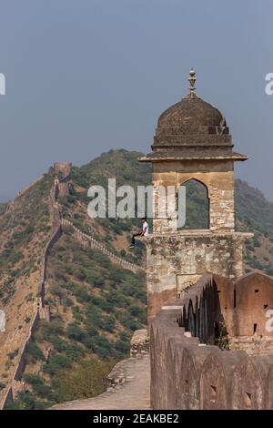 Young Boy sitzt auf Wachturm von Amber Fort mit Wand und Stadtmauer Hintergrund, Jaipur, Rajasthan, Indien. Stockfoto