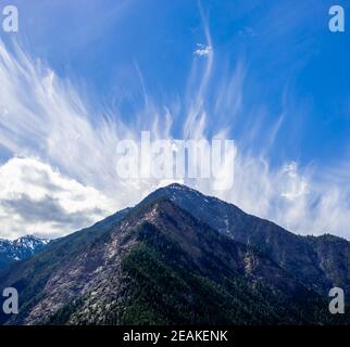 Cirrus Wolken breiten sich in den Himmel über dem Berg aus. Stockfoto