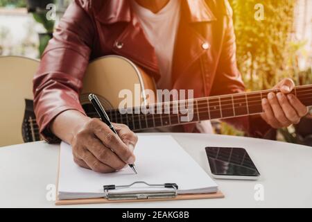 Ein Songwriter hält Stift für ein Lied zu komponieren. Musiker spielt akustische Gitarre. Live-Musik und abstraktes musikalisches Konzept. Stockfoto