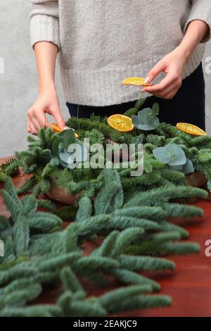 Das Mädchen macht einen Kranz für das neue Jahr oder Weihnachten. Ein traditionelles Accessoire. Fotos ohne Gesichter. Stockfoto