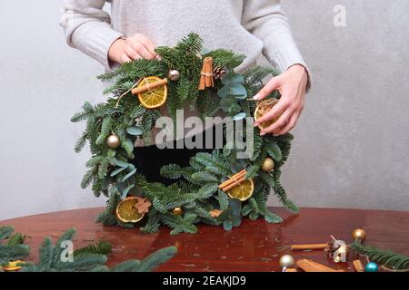 Die Hände des Mädchens halten einen Kranz für das Neue Jahr aus den Zweigen der dänischen Fichte und Eukalyptus. Fotos ohne Gesicht. Nur Hand. Speicherplatz kopieren. Konzept von Traditionen und Urlaub. Stockfoto