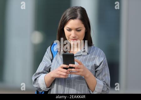 Student überprüft Smartphone zu Fuß in einem Campus Stockfoto