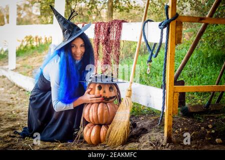 Ein Mädchen in einem Hexenkostüm, feiert Halloween, setzte sich von einem Kürbis mit einem gezeichneten bösartigen Grimasse Stockfoto