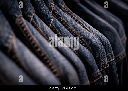 Selektiver Fokus auf Jacke Jeans hängen auf Rack im Bekleidungsgeschäft. Jeans mit Jeans-Muster. Textilindustrie. Jeans Mode und Shopping Konzept. Bekleidungskonzept. Jeansjacke auf Rack zum Verkauf. Stockfoto
