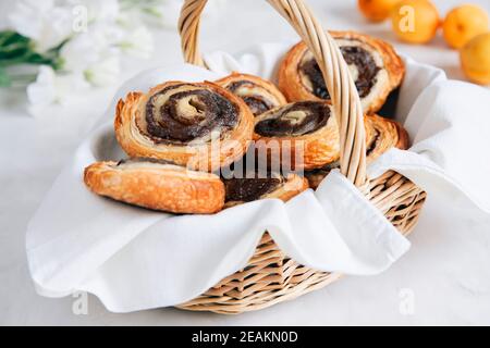 Knusprige Blätterteigbrötchen mit Zucker und Zimt in einem Weidenkorb auf einem Tisch. Süßes Frühstück. Stockfoto