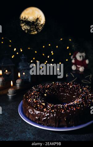 Weihnachten hausgemachten dunklen Schokolade gebündelt Kuchen auf einem blauen Teller mit Schokolade Glasur und bunten Zucker bestreut dekoriert. Stockfoto