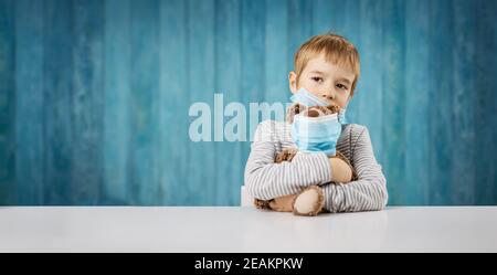 Kleiner Junge, der mit einem Teddybären im medizinischen Gesicht sitzt Masken Stockfoto