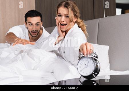 Besorgte Frau und muslimischer Mann, der den Wecker ansieht Verschwommener Vordergrund im Hotel Stockfoto