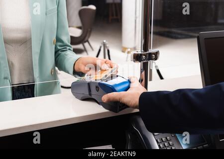 Kurzer Blick auf die Frau, die mit Kreditkarte bezahlt, während die Empfangsdame an der Rezeption ist Halteterminal im Hotel Stockfoto