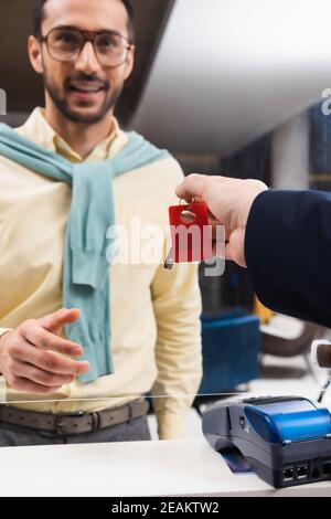 Der Hotelmanager hält den Schlüssel in der Nähe des Zahlungsterminals und lächelt muslimisch Mann auf unscharfem Hintergrund Stockfoto