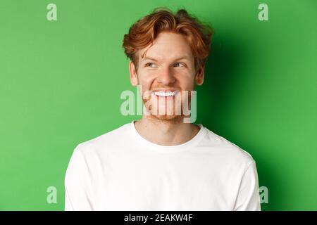 Headshot von glücklich Rotschopf Mann mit Bart tragen weißen langen Ärmeln, Blick links auf Kopie Raum und lächelnd, stehend auf grünem Hintergrund Stockfoto