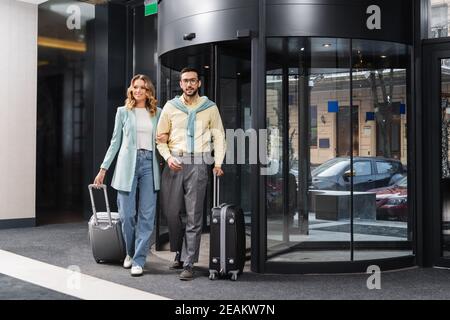 Lächelndes interrassisches Paar, das mit Koffern in der Nähe des Hotels läuft Stockfoto