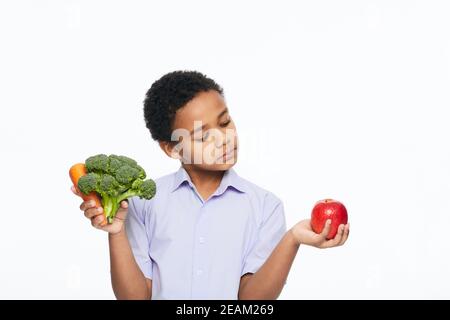 Der afroamerikanische Junge hält Karotten, Brokkoli und Apfel in der Hand. Gesund essen für Kinder Stockfoto