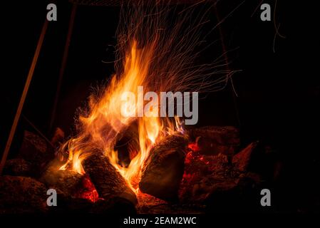 Nachtlager mit verfügbarem Platz. Großes Lagerfeuer vor schwarzem Hintergrund. Funken von Lagerfeuer und Feuer aus der Nähe Stockfoto