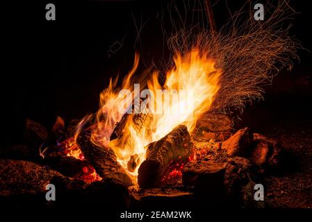 Nachtlager mit verfügbarem Platz. Großes Lagerfeuer vor schwarzem Hintergrund. Funken von Lagerfeuer und Feuer aus der Nähe Stockfoto