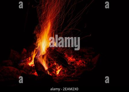 Nachtlager mit verfügbarem Platz. Großes Lagerfeuer vor schwarzem Hintergrund. Funken von Lagerfeuer und Feuer aus der Nähe Stockfoto