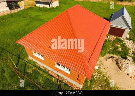 Haus mit einem orangefarbenen Dach aus Metall, Ansicht von oben. Metallische Profil gestrichen Wellpappe auf dem Dach. Stockfoto