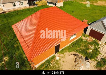 Haus mit einem orangefarbenen Dach aus Metall, Ansicht von oben. Metallische Profil gestrichen Wellpappe auf dem Dach. Stockfoto