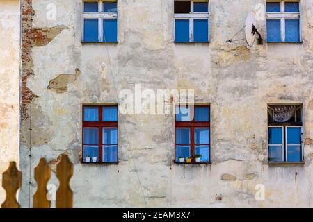 Schäbige rissige Wand, alte Fenster, Armutskonzept. Vorderfassade des alten Apartmentgebäudes Stockfoto