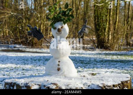 Niedlicher Schneemann aus drei Schneebällen mit Blättern für Haare, Zweige für Arme mit Kinderhandschuhen, Tannenzapfen für Nase und Steine für Knöpfe. Stockfoto