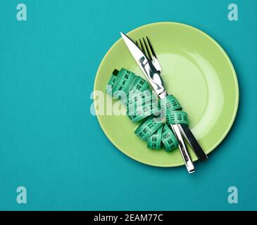 Grüne runde Platte und Gabel und Messer in grün eingewickelt Maßband auf blauem Hintergrund Stockfoto