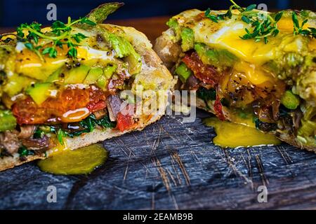 Vegetarisch beladen Brote gefüllt mit langsam gerösteten Tomaten, Spinat, Lauch, Austernpilze, Avocado, Spargel, bestreut mit Käse und gekrönt Stockfoto