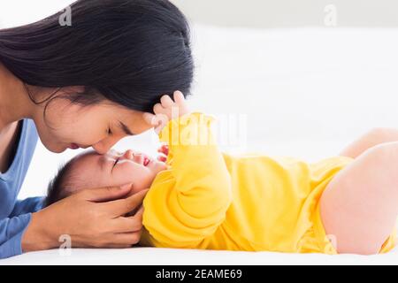 Mutter küsst ihr neugeborenes Baby in einem weißen Bett Stockfoto