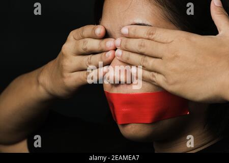 Asiatische Frau Augenbinde wickeln Mund mit rotem Klebeband Stockfoto