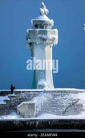 Sassnitz, Deutschland. Februar 2021, 10th. Ein Mann fotografiert den eisigen Leuchtturm am Pier des Hafeneingangs. Eisige Witterung und Schneefall behindern den Verkehr in Norddeutschland. Quelle: Jens Büttner/dpa-Zentralbild/dpa/Alamy Live News Stockfoto