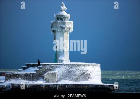 Sassnitz, Deutschland. Februar 2021, 10th. Ein Mann fotografiert den eisigen Leuchtturm am Pier des Hafeneingangs. Eisige Witterung und Schneefall behindern den Verkehr in Norddeutschland. Quelle: Jens Büttner/dpa-Zentralbild/dpa/Alamy Live News Stockfoto