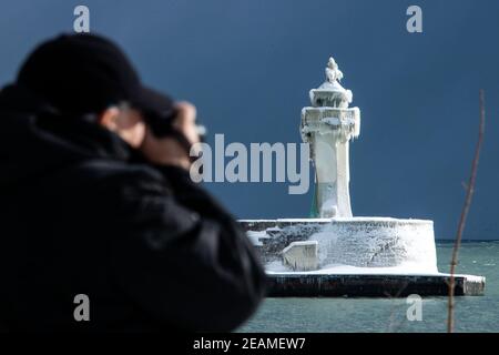 Sassnitz, Deutschland. Februar 2021, 10th. Ein Mann fotografiert den eisigen Leuchtturm am Pier des Hafeneingangs. Eisige Witterung und Schneefall behindern den Verkehr in Norddeutschland. Quelle: Jens Büttner/dpa-Zentralbild/dpa/Alamy Live News Stockfoto