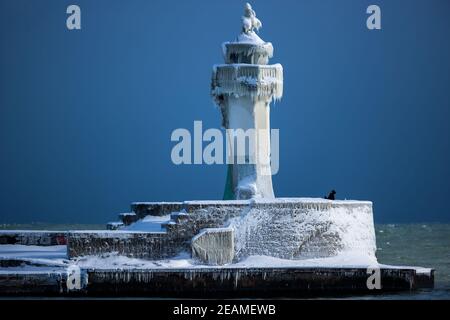 Sassnitz, Deutschland. Februar 2021, 10th. Ein Mann fotografiert den eisigen Leuchtturm am Pier des Hafeneingangs. Eisige Witterung und Schneefall behindern den Verkehr in Norddeutschland. Quelle: Jens Büttner/dpa-Zentralbild/dpa/Alamy Live News Stockfoto