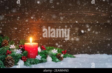 Weihnachten oder Advent Holzhintergrund mit brennender roter Kerze auf Schnee und Schneeflocken, verziert mit Tannenzweigen und Ornamenten. Speicherplatz Kopieren Stockfoto
