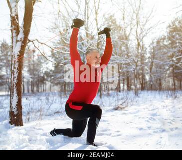 Funktionelles Fitness-Workout im Freien. Reifer Mann mit Bodyweight Widerstand Riemen, dabei Ausfallschritte im verschneiten Winter Park Stockfoto