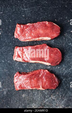Scheiben rohes Striploin Steak auf schwarzem Küchentisch. Stockfoto