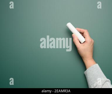 Hand hält ein Stück weiße Kreide auf dem Hintergrund Von einem leeren grünen Kreidetafel Stockfoto