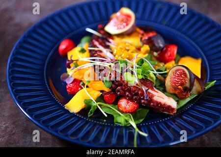 Octopus Salat mit Mango und Erdbeeren auf einem blauen Teller. Fotos ohne Personen. Kochkonzept. Stockfoto
