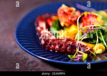 Nicht fokussiert. Octopus Salat mit Mango und Erdbeeren auf einem blauen Teller. Fotos ohne Personen. Kochkonzept. Stockfoto