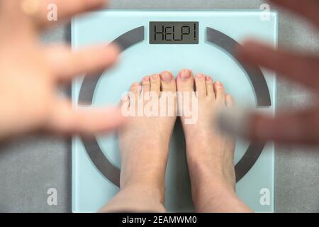 Person Füße auf digitale Waage mit den Worten helfen, besorgte Hände zeigen, Top-Ansicht Ernährung und Gesundheit Konzept Stockfoto