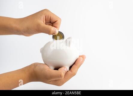 Ein Sparschwein in der Hand und setzt Münzen in ein Sparschwein mit Kopierraum auf weißem Hintergrund. Stockfoto